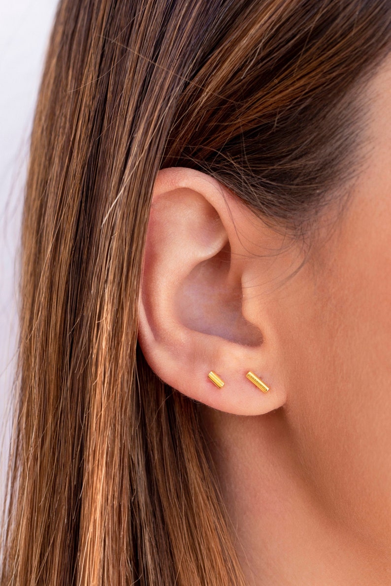 May include: A pair of gold bar stud earrings. The earrings are small and simple, and they are a classic style that can be worn with any outfit.