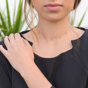 May include: A woman wearing a black top with a silver choker necklace with small round charms.