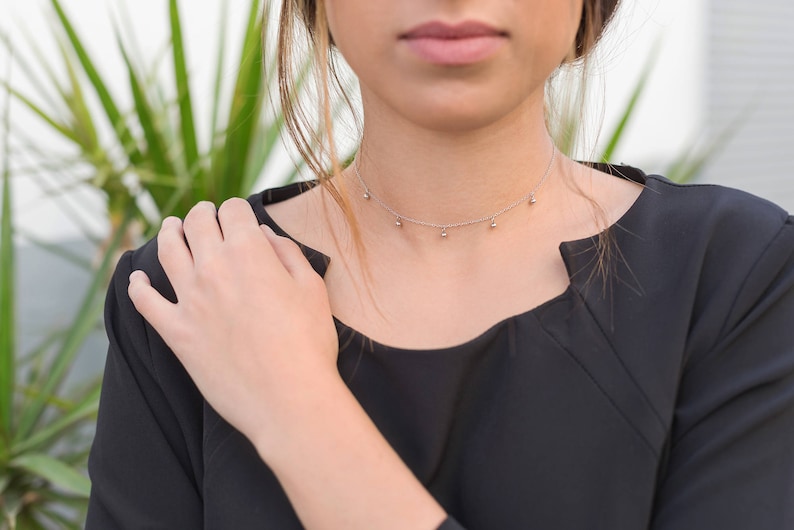 May include: A woman wearing a black top with a silver choker necklace with small round charms.