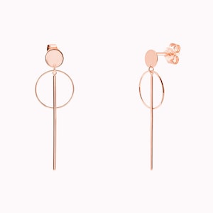 May include: Rose gold earrings with a circle and a long, thin rod hanging from a small round disc.