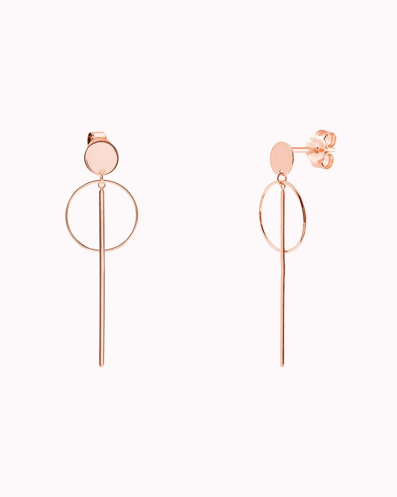 May include: Rose gold earrings with a circle and a long, thin rod hanging from a small round disc.