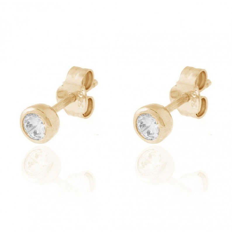 May include: A pair of gold stud earrings with a clear round stone in the center.