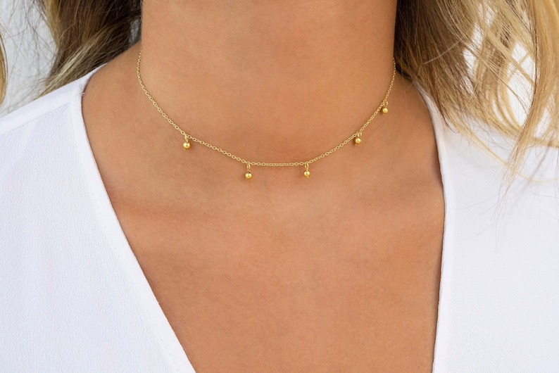 May include: A gold chain choker necklace with five small gold balls hanging from it.