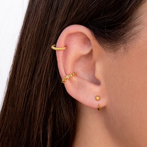 Puede incluir: Pendientes de aro de oro con un dise&ntilde;o texturizado. El aro se lleva en la parte superior de la oreja. Un peque&ntilde;o pendiente de bot&oacute;n de oro se lleva en el l&oacute;bulo inferior de la oreja. Un aro de oro se lleva en el l&oacute;bulo inferior de la oreja.