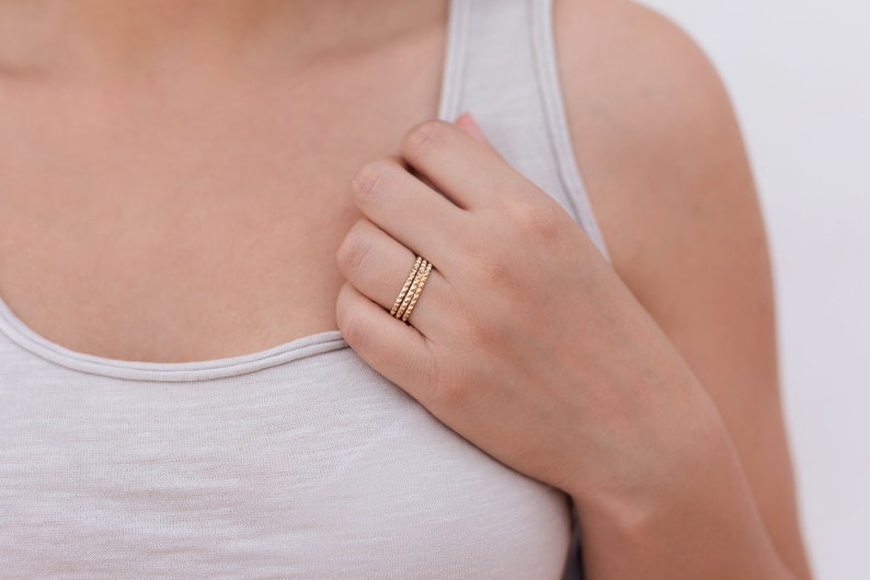 May include: A close-up of a hand wearing three gold beaded rings.