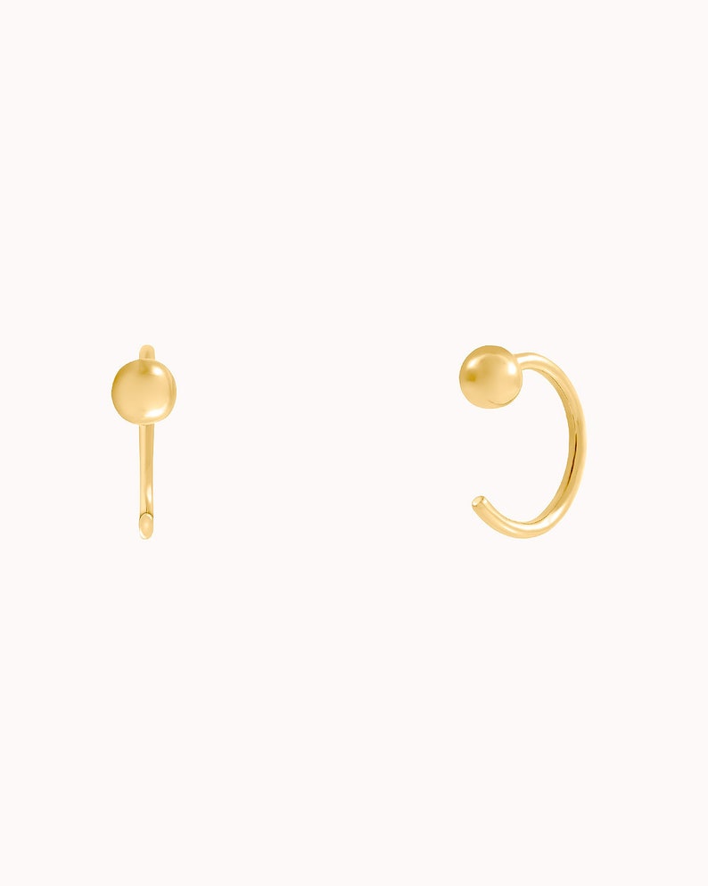 Puede incluir: Un par de pendientes de aro de oro con una peque&ntilde;a bola en el extremo de cada aro.