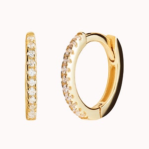 May include: A pair of gold hoop earrings with a row of small clear stones around the edge.