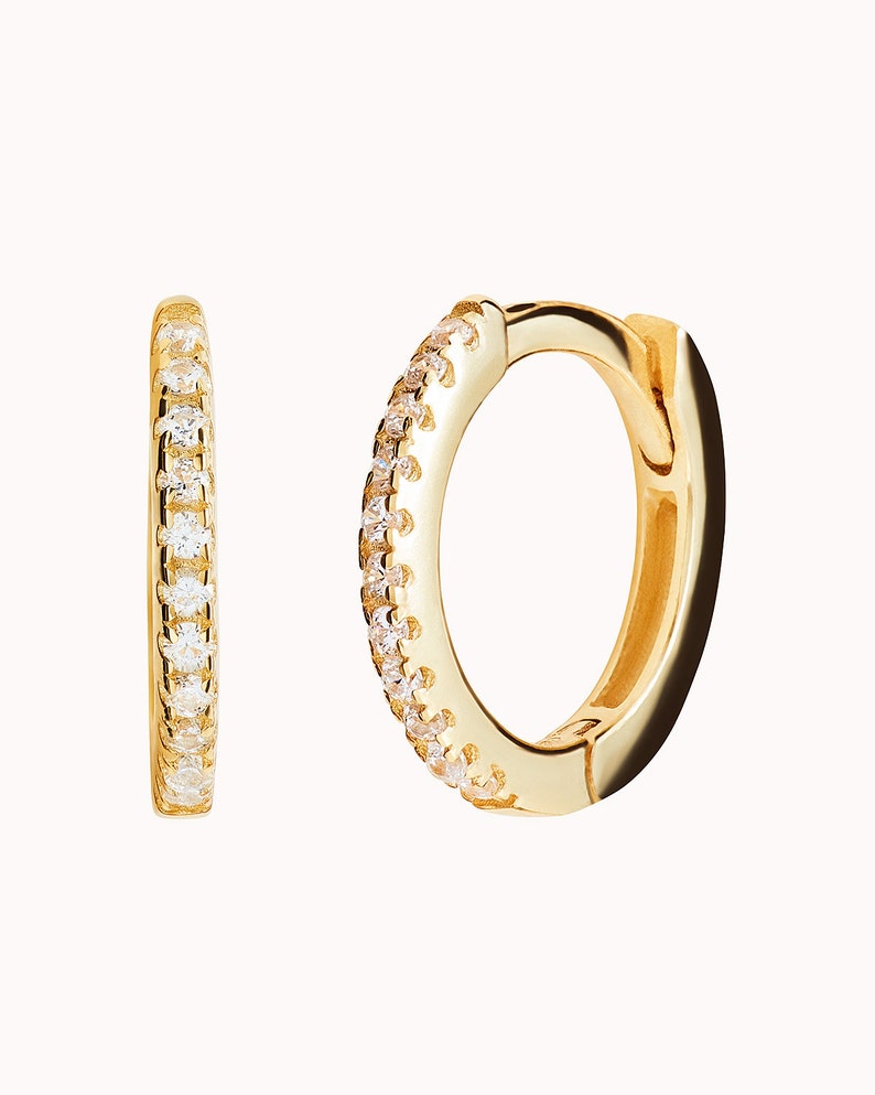 May include: A pair of gold hoop earrings with a row of small clear stones around the edge.