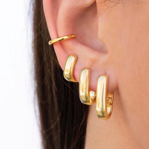 Può includere: Tre orecchini a cerchio d'oro di diverse dimensioni. L'anello più grande ha un diametro di circa 2,5 cm, l'anello intermedio ha un diametro di circa 2 cm e l'anello più piccolo ha un diametro di circa 1,25 cm.
