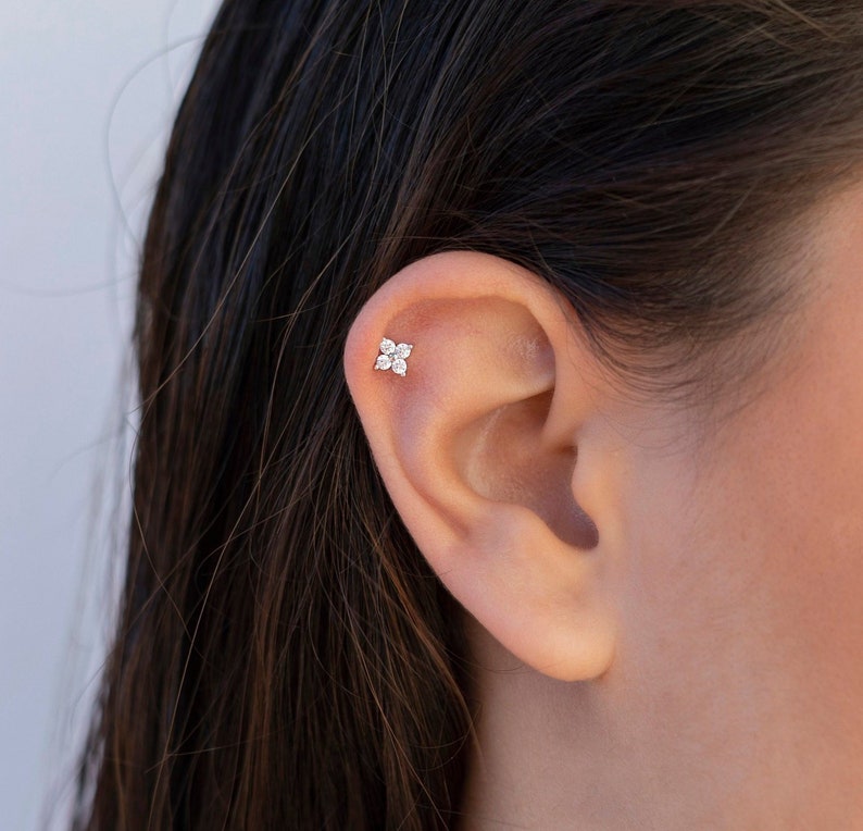 Puede incluir: Primer plano de una oreja con un peque&ntilde;o pendiente de plata con forma de flor con cinco piedras preciosas transparentes.