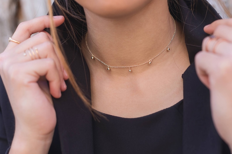 May include: A gold chain choker necklace with small round beads hanging from it.