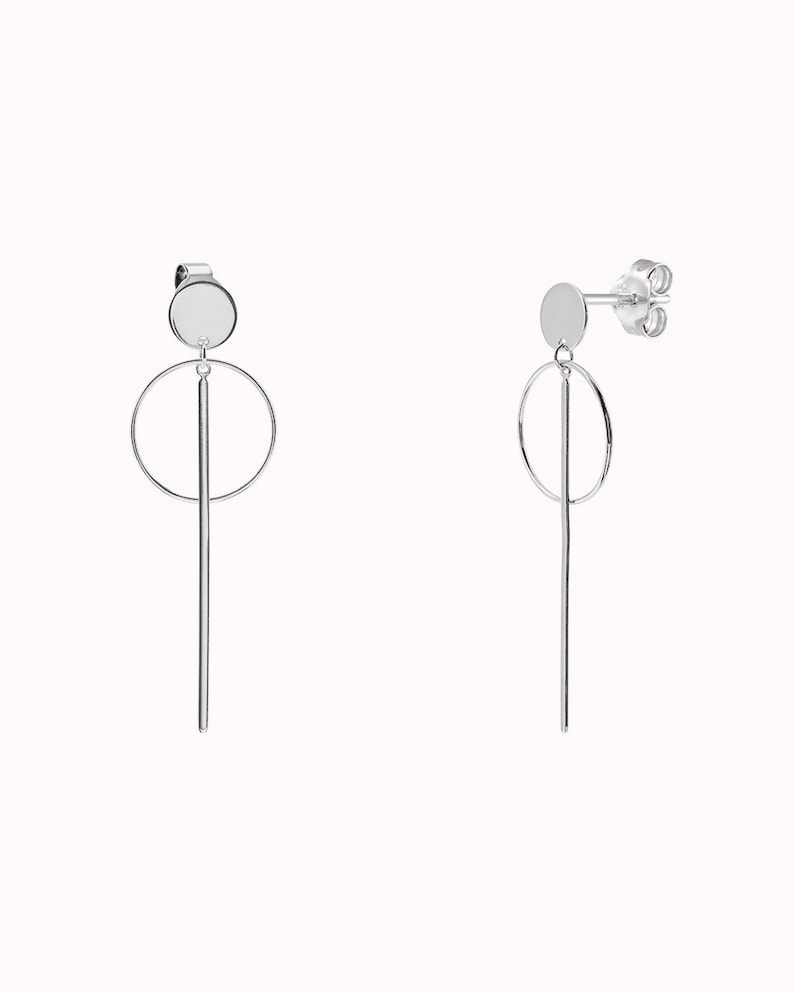 May include: A pair of silver earrings with a circle and a long, thin rod hanging from a small round disc.