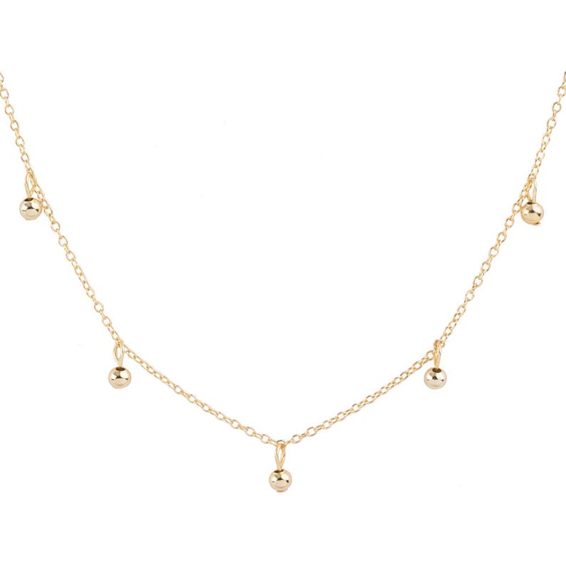 May include: A gold chain necklace with five small gold balls hanging from it.