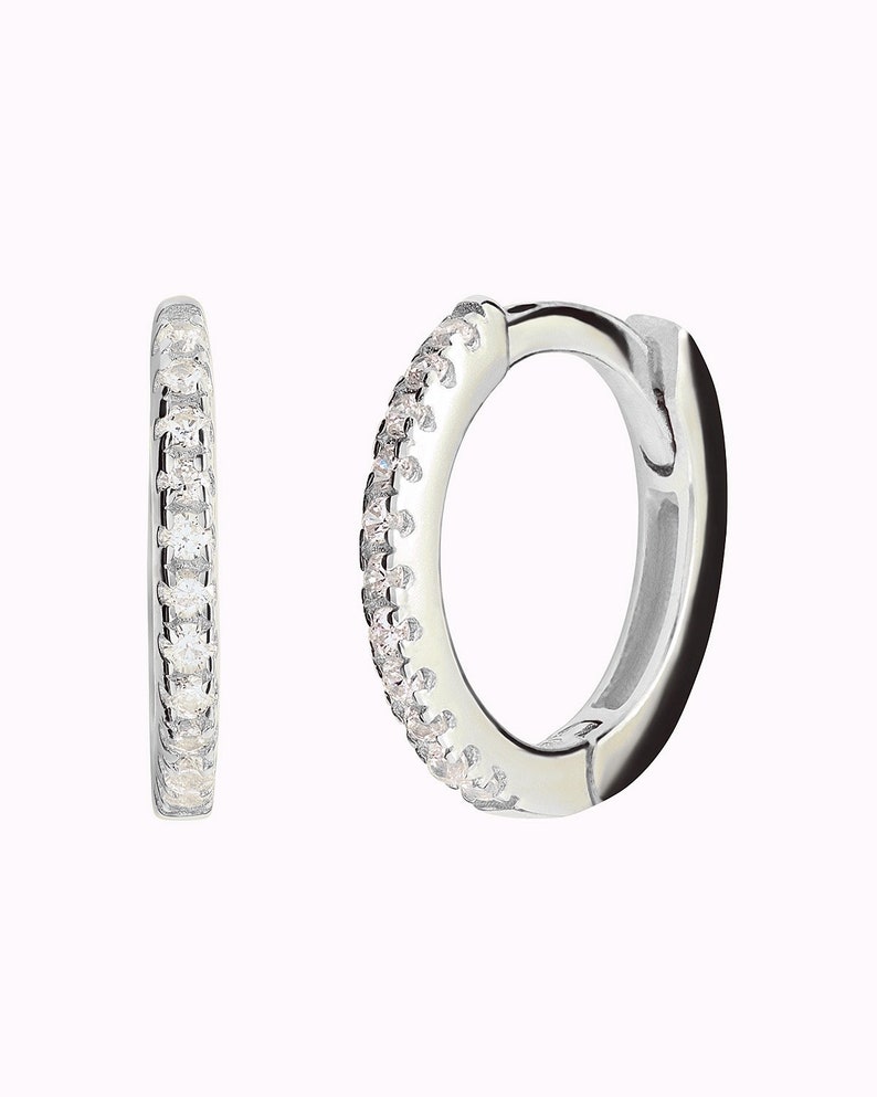 May include: A pair of silver hoop earrings with a row of small clear cubic zirconia stones around the edge.