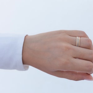 May include: A close-up of a hand wearing three gold stacking rings with small beads.