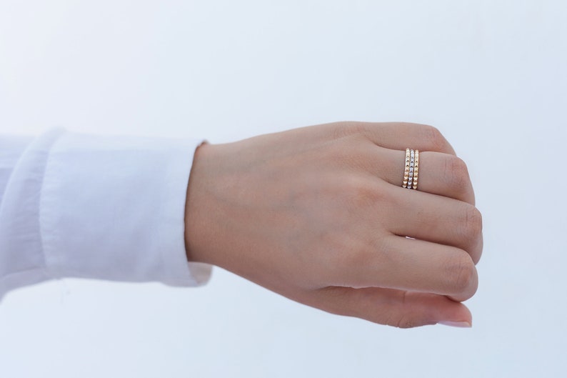 May include: A close-up of a hand wearing three gold stacking rings with small beads.