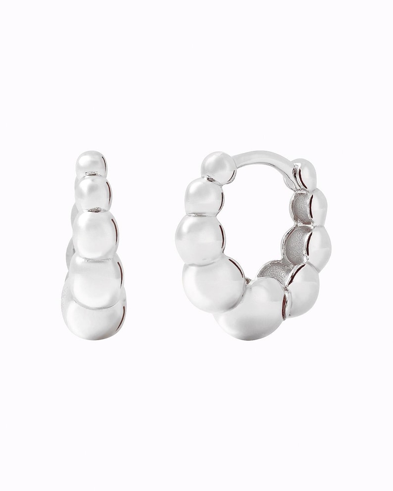 Pu&ograve; includere: Un paio di orecchini a cerchio d'argento con un design a perline. Gli orecchini sono realizzati con piccole perline rotonde che sono collegate tra loro per formare una forma a cerchio.