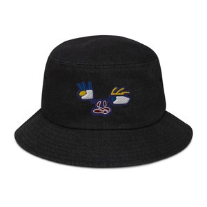 Puede incluir: Sombrero de pescador negro con un diseño de cara bordada de colores. La cara tiene dos ojos, una nariz y una boca.