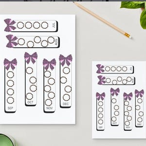 May include: White paper with a decorative design featuring purple glitter bows and circular patterns. The months of July, August, September, October, November, and December are labeled. A pencil rests on the surface.
