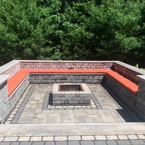 May include: A brick patio with a fire pit in the center. The patio is surrounded by a brick wall with red cushions. The wall has a sign that says "Fire Pit".