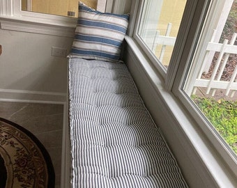 May include: A white and blue striped window seat cushion with a blue and white striped pillow on top. The cushion is tufted and has a thick, comfortable look.