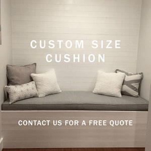 May include: A gray window seat cushion with three decorative pillows. The seat cushion is in a built-in window seat. The text "CUSTOM SIZE CUSHION" is displayed above the seat cushion. The text "CONTACT US FOR A FREE QUOTE" is displayed below the seat cushion.
