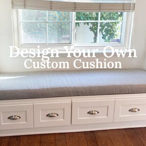 May include: A long, rectangular light gray fabric cushion placed on a white built-in window bench with four drawers featuring silver cup pulls. The text "Design Your Own Custom Cushion" is overlaid in white letters across the center of the image.