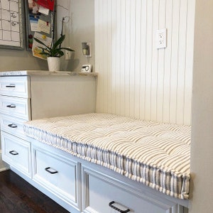 May include: White built-in bench with a striped cushion and drawers. The bench is in a kitchen or mudroom.