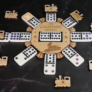 May include: A wooden domino game set with the text "THE QUESENBERRY EXPRESS". The set includes dominoes with colored dots and wooden train cutouts with names. The game is arranged on a dark surface.