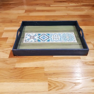 May include: A black wooden serving tray with a green liner and a decorative tile design in blue, white, and yellow.