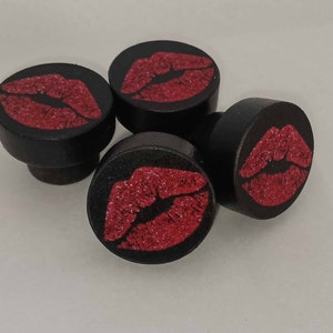 May include: Four black wooden bottle stoppers with red glitter lips printed on the top.