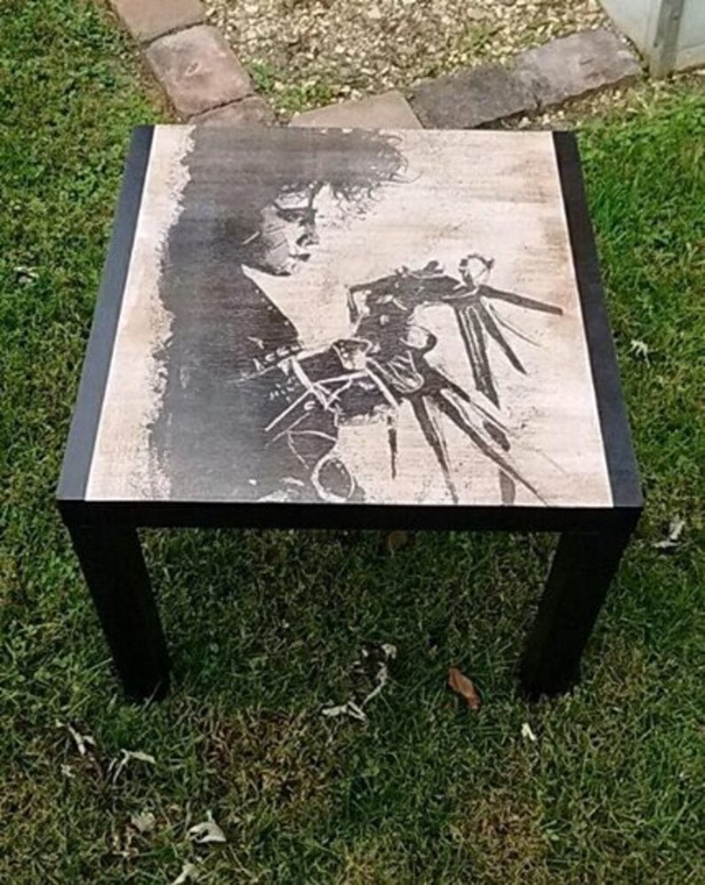 May include: Black and white image of a character from the film Beetlejuice on a square coffee table with black legs.