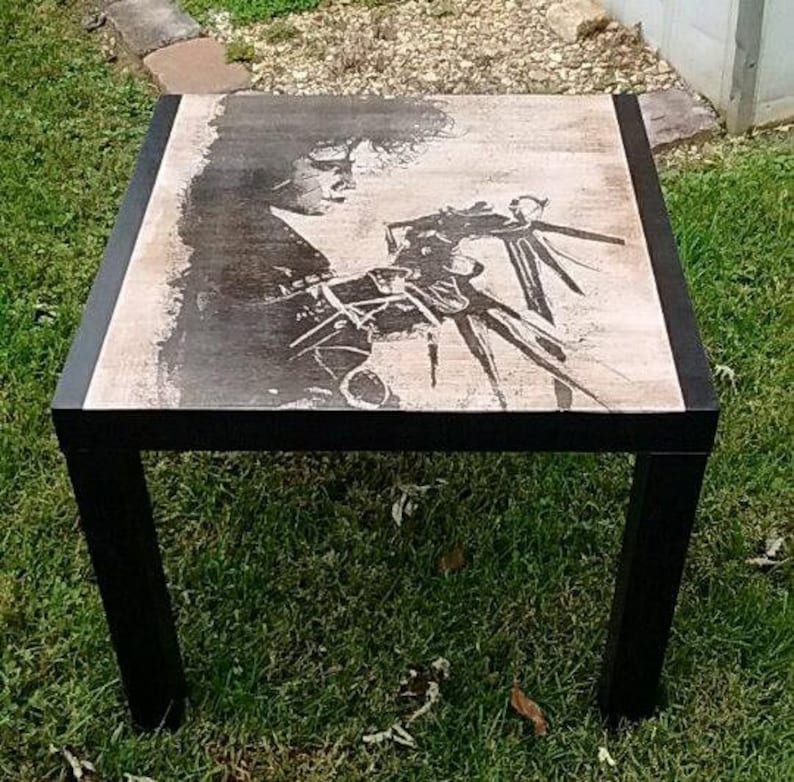May include: Black coffee table with a square top featuring a black and white image of a person with a large hand. The table has a black frame.