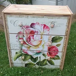 Puede incluir: Cómoda de madera con tres cajones. Los cajones presentan un gran diseño floral de rosas rosas y rojas con hojas verdes. El texto "Collection" y "Post Card" son visibles.