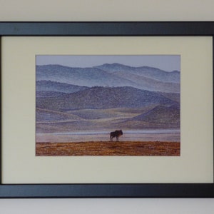 Puede incluir: Una impresión enmarcada de un ñu blanco y negro de pie en un campo con una cadena montañosa brumosa en el fondo.