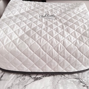 May include: White quilted appliance cover with a gray trim and the word "Bella" embroidered in black.