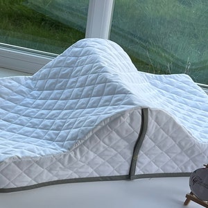 May include: White quilted cushion with a gray trim. The cushion is shaped like a wedge and is designed to be used as a support for a person's back or legs.