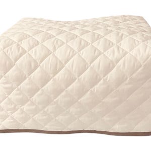 May include: A cream-colored quilted cover for a small appliance, such as a toaster oven or coffee maker. The cover has a diamond-shaped quilting pattern and a brown trim around the edges.