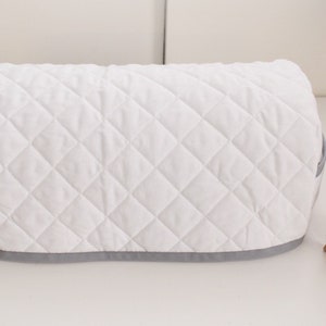 May include: White quilted sewing machine cover with a grey trim. The cover is designed to protect a sewing machine from dust and dirt.