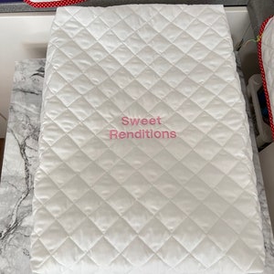 May include: White quilted fabric cover with a pink embroidered logo that says "Sweet Renditions".