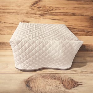 May include: A white quilted appliance cover featuring a diamond-shaped stitched pattern across the entire surface. The cover has a structured, rectangular shape with a smooth, finished bottom edge, designed to fit over kitchen equipment.
