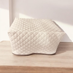 May include: A cream-colored, quilted appliance cover featuring a diamond-stitched pattern across its entire surface. The cover has a structured, rectangular shape with a flat top and slightly tapered sides, finished with a solid-colored bottom trim.