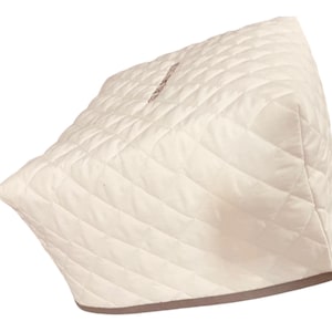 May include: A cream-colored, quilted appliance cover featuring a diamond-stitched pattern across its exterior. The cover has a structured, boxy shape with a solid, darker-toned trim along the bottom edge, designed to fit over a kitchen appliance.