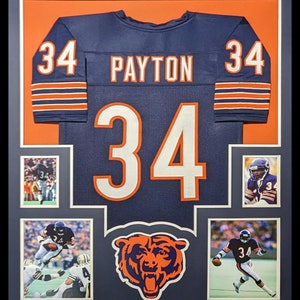 May include: A framed Chicago Bears jersey with the name "PAYTON" and the number "34" on the back. The jersey is blue with orange and white stripes. The frame includes four smaller photos of Walter Payton in action.