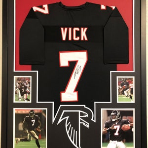 May include: A framed black Atlanta Falcons jersey with the name "VICK" and the number "7" on the back. The jersey is signed by Michael Vick. The frame includes four smaller photos of Vick in action.