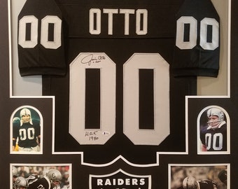 May include: A framed black and white football jersey with the name "OTTO" and the number "00" on the front. The jersey is signed by the player and includes a Raiders logo and photos of the player in action.