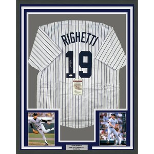 May include: A framed white and blue baseball jersey with the name "Righetti" and the number "19" on the back. The jersey is signed by Dave Righetti, a former New York Yankees pitcher. The frame includes two smaller photos of Righetti pitching.