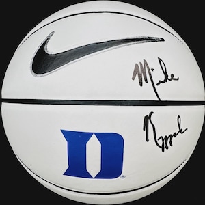 Peut inclure: Ballon de basket blanc avec un logo Nike noir et le logo de l'Université Duke en bleu. Comporte deux signatures à l'encre noire. Le ballon a des coutures noires.