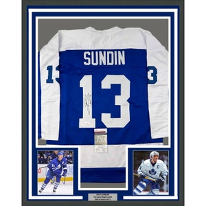 May include: Framed Toronto Maple Leafs hockey jersey, featuring the name "SUNDIN" and the number "13" in white on a blue and white jersey. Includes photos of the player and a plaque that reads "MATS SUNDIN Toronto Maple Leafs Hall of Fame 2012".
