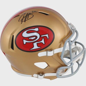 May include: A gold-colored football helmet with a red stripe and the San Francisco 49ers logo. The logo is a red oval with the letters "SF" in white. The helmet has a gray face mask and a signature on top.